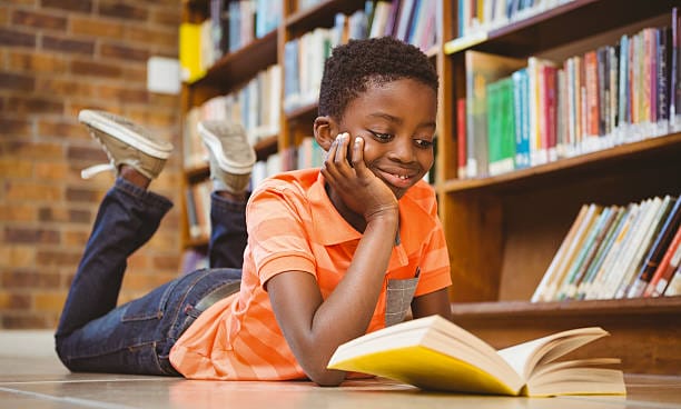 صبي صغير لطيف يقرأ كتاباً في المكتبة